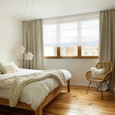 a bed sitting in a bedroom next to a window with drapes on the windowsill