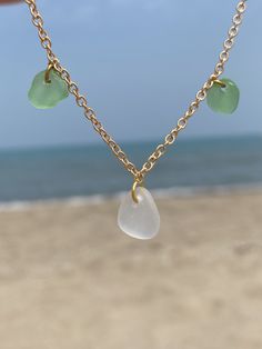 a person is holding a necklace with sea glass charms on it and the ocean in the background