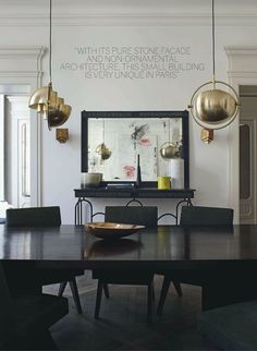 the dining room table is surrounded by black chairs and gold pendant lights hanging from the ceiling