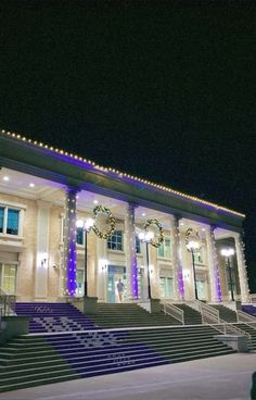 a large building with stairs and lights on it's sides at night time in the snow