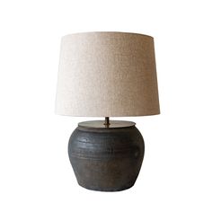 a lamp that is sitting on top of a white surface with a beige shade over it