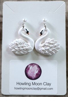 pair of white swan earrings on card with logo for the howling moon clay studio, inc