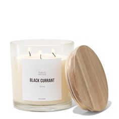 a white candle with a wooden lid sitting next to a glass jar filled with black curran