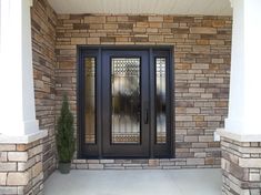 the front door to a home with glass panels and stone columns on either side,