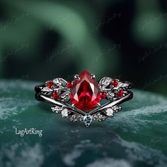 a close up of a ring with a red stone in the center and leaves around it