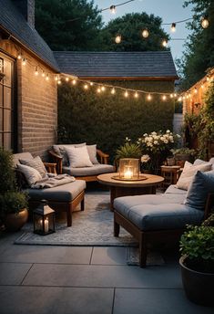 an outdoor patio with lights strung over the seating area and table, surrounded by potted plants