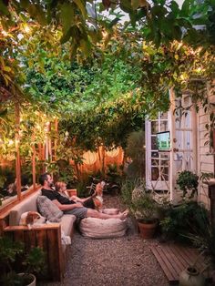 two people sitting on a couch in the middle of a garden with trees and plants