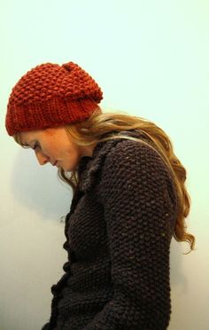 a woman wearing a red knitted hat looking down at her cell phone while leaning against a wall