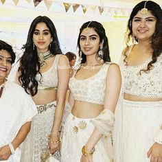 three women in white outfits standing next to each other at a wedding ceremony with one woman wearing a sari and the other holding a purse