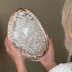 a woman is holding a glass dish with ice on it and looking at the mirror