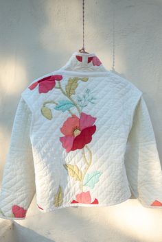 a white quilted jacket hanging from a hook on a wall with flowers painted on it