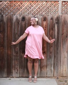 a woman standing in front of a wooden fence with her arms spread out and smiling