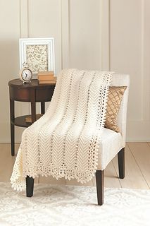 a white crocheted blanket sitting on top of a chair next to a table