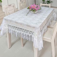 the table is covered with white lace and has pink flowers in a vase on it