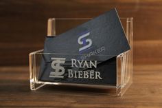 a clear acrylic business card holder on a wooden table with the name ryan bieber