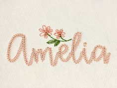 an embroidered name on a white shirt with pink flowers and green leaves in the center