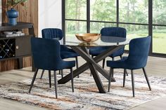 a dining room table with blue chairs and a gold bowl on the glass top, in front of a large window