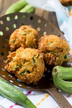 three fried food items in a colander on a table with green beans and a fork