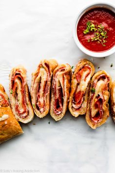 several sandwiches with meat and cheese on them next to a bowl of tomato sauce