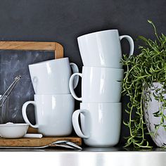 there are many white cups and bowls on the counter next to a chalk board with a blackboard behind it