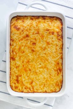 a white casserole dish filled with cheese on top of a striped towel next to a fork