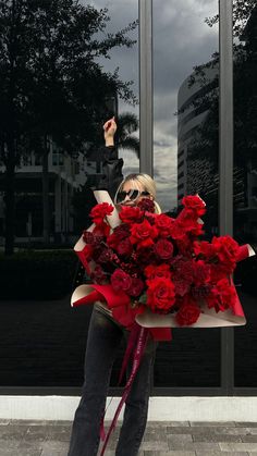 a woman holding a bouquet of red roses in front of a building with large windows