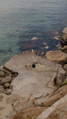 there is an umbrella and chairs on the rocks by the water with no one around it