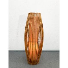 a tall bamboo vase sitting on top of a cement floor next to a white wall