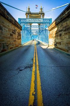 an empty road with a blue bridge in the background and yellow lines painted on it