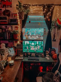 a computer desk with a cat sitting on it in front of a window covered by christmas lights