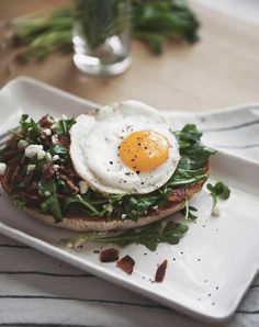 an egg is sitting on top of a toasted bun with greens and bacon around it