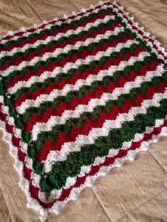 a crocheted blanket is laying on the floor with red, green and white stripes