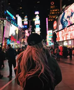 a woman with long hair standing in the middle of a busy city street at night