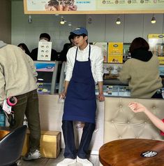 a man wearing an apron standing in front of a counter at a restaurant with customers