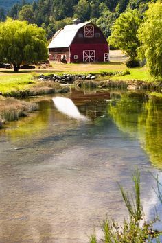 a red barn sitting on the side of a lush green field next to a river