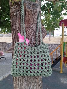 a crocheted bag hanging from a tree in front of a playground with swings