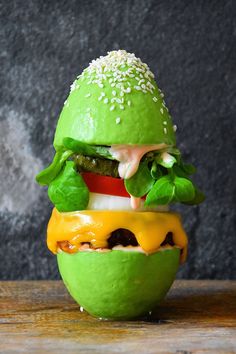 a green hamburger with cheese, lettuce and tomato on it sitting on a wooden table