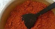 a wooden spoon in a bowl filled with red seasoning next to a white tablecloth