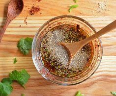 a wooden spoon and some spices in a glass bowl on a table with parsley