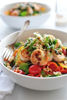 a white bowl filled with shrimp and veggies next to a fork on top of a table