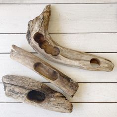 three driftwood pieces with holes in them on a white wooden surface