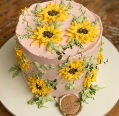 a pink cake with sunflowers on it and a penny sitting next to it