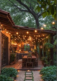 an outdoor dining area with lights strung from the ceiling and wooden table surrounded by greenery