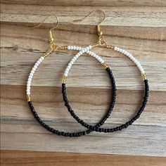 two black and white beaded hoop earrings with gold accents on a wooden table top