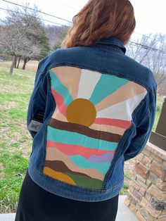 a woman standing in front of a brick wall wearing a jean jacket with an abstract painting on it