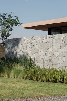 a large stone wall next to a building with grass and trees in front of it