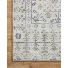 a white rug with blue and grey flowers on the bottom, in front of a wooden floor