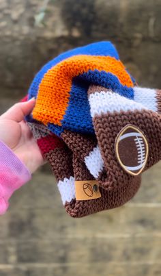 a hand is holding three knitted sports mitts in different colors and patterns, one with a football on it