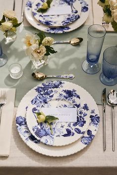 a table set with blue and white plates, silverware and flowers in vases