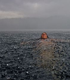 a woman swimming in the ocean with her head above the water's surface and dark clouds overhead